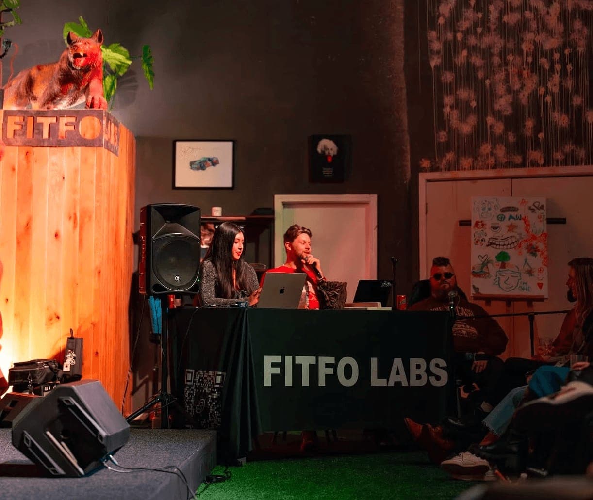 Performers behind a Fitfo Labs banner in a wood-panelled room, with the audience close by, Nite in the Lab