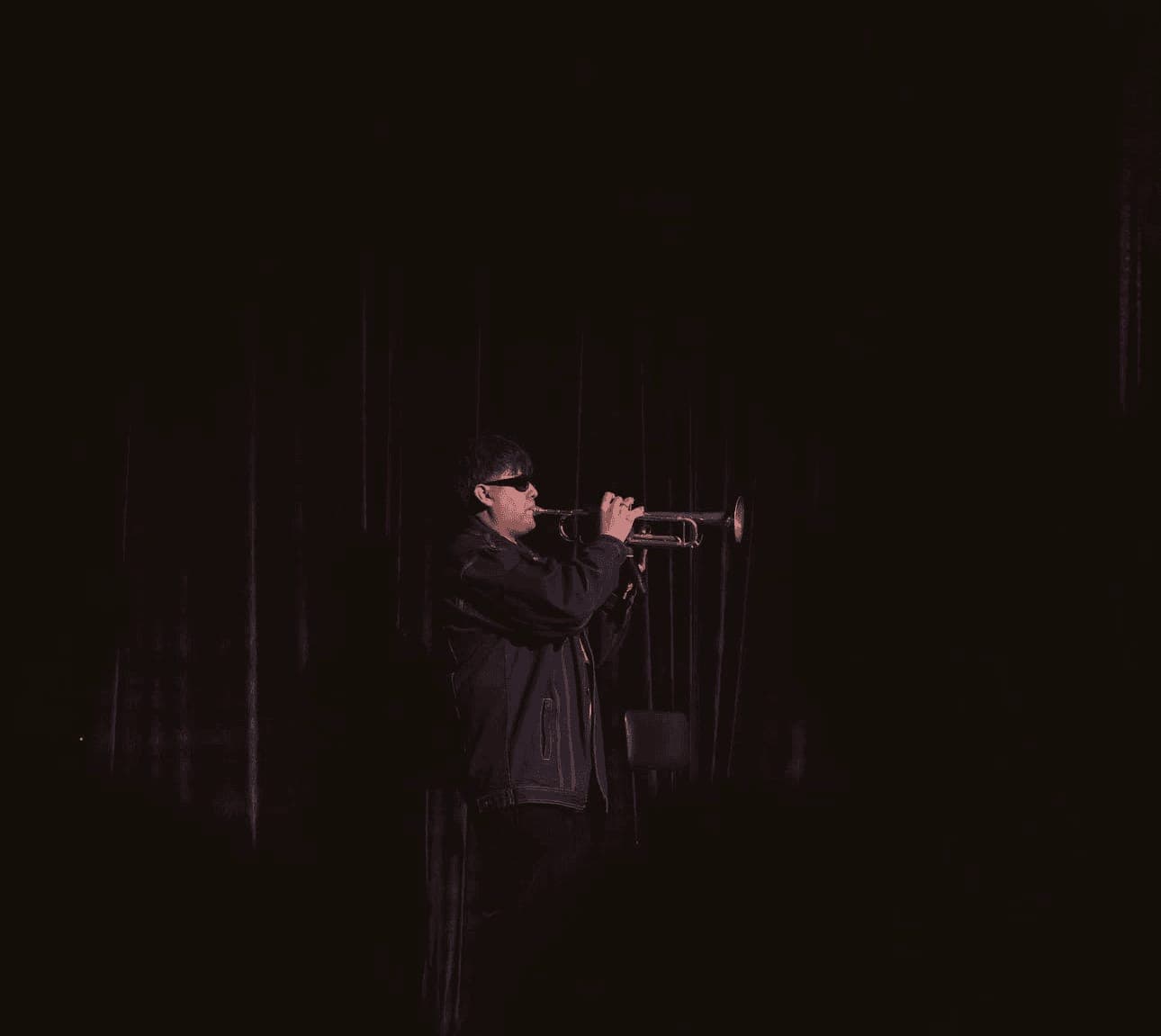 A trumpet player performs in near darkness