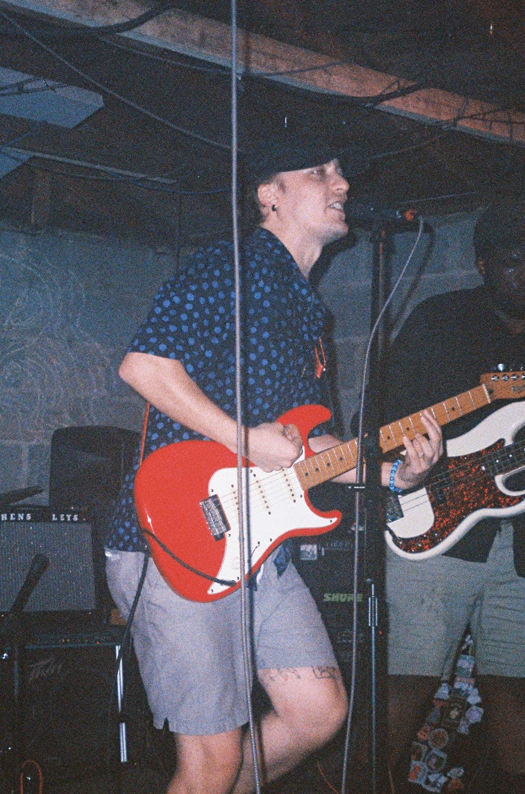 A guitarist plays a red electric guitar at an outdoor night show