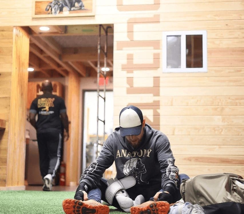A man sits on the turf floor of a wood-built studio space