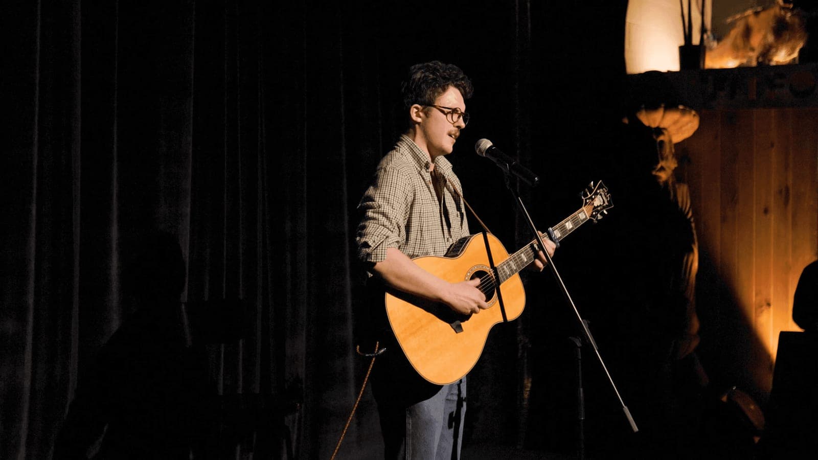 A singer plays acoustic guitar on a dim stage, Nite in the Lab